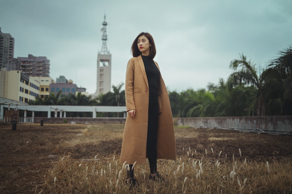 donna che indossa cappotto marrone in piedi su erba marrone