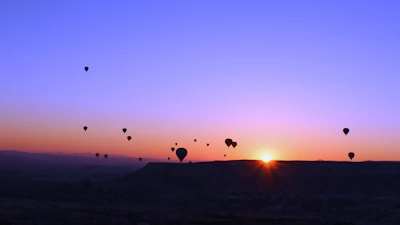 A hot air balloon soaring gently over a lush green landscape at sunrise.
