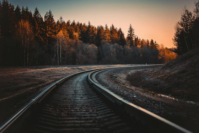 Modern railway track winding through mountainous landscape at sunrise.
