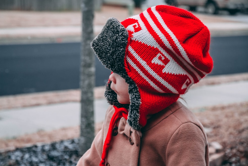 toddler wearing red and white knit hat near road during daytime