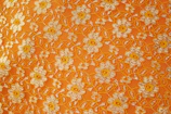 Artisan sewing vibrant orange lilies onto a sandy-colored textile.