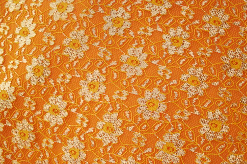 Artisan sewing vibrant orange lilies onto a sandy-colored textile.