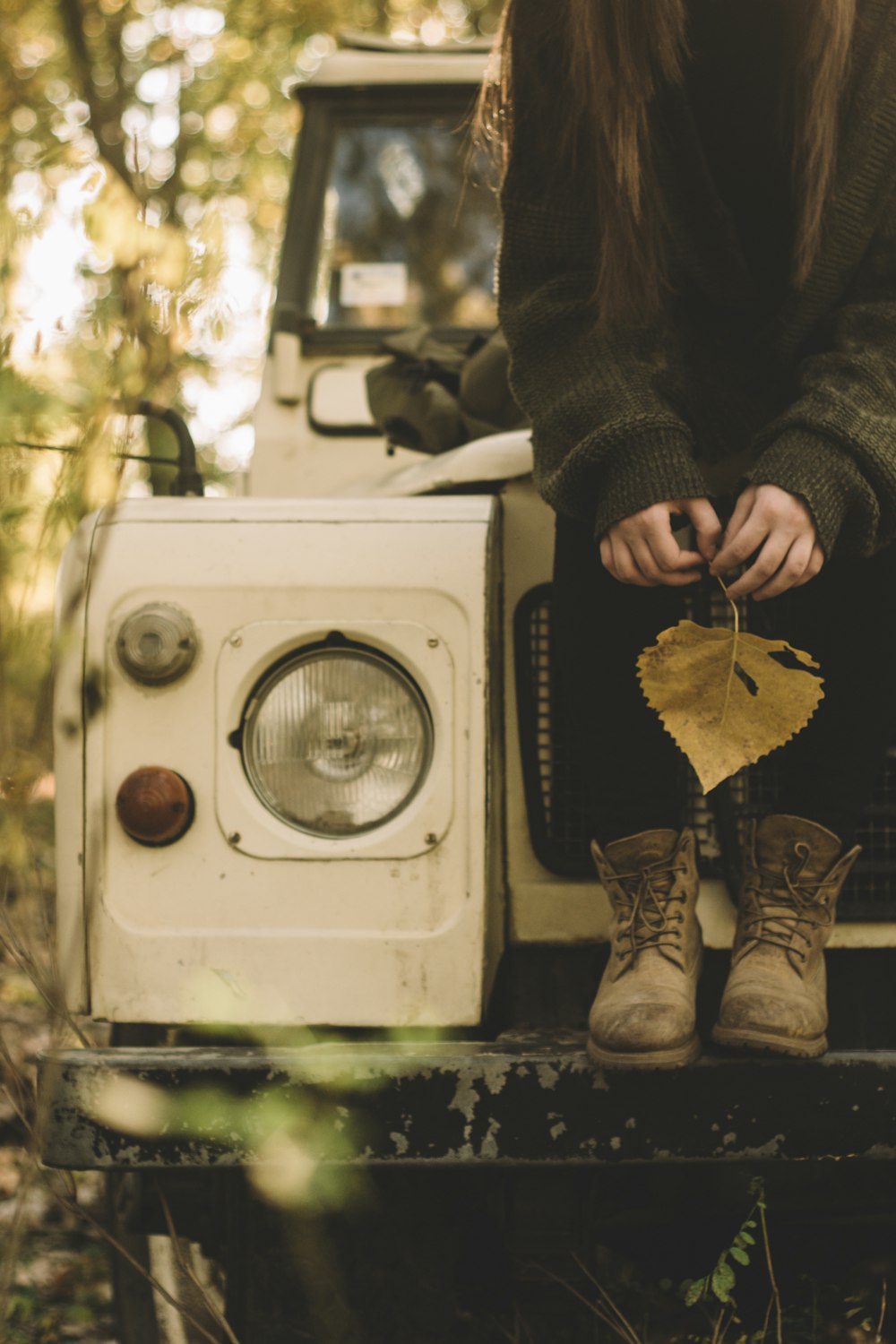 woman in gray sweater holding withered leaf while sitting on white vehicle