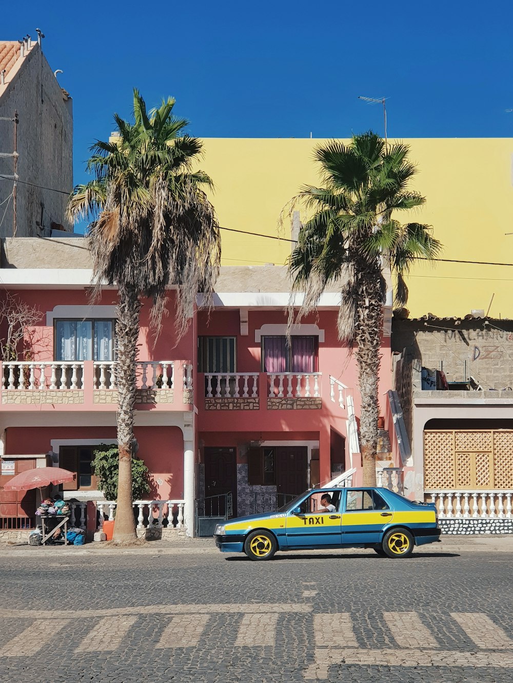 Blaues und gelbes Taxi in der Nähe von Palme geparkt