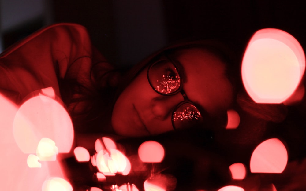 bokeh photography of woman wearing eyeglasses while lying