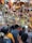 A crowded marketplace filled with vibrant and colorful hanging decorations, including bells, beads, and crafts. Many people are browsing through the lively and festive items displayed above and around them.