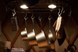 Shiny pots and pans hanging from a kitchen rack with warm lighting.