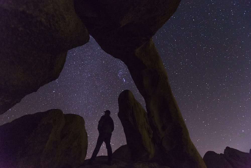 silhouette of person under rock formation at night time