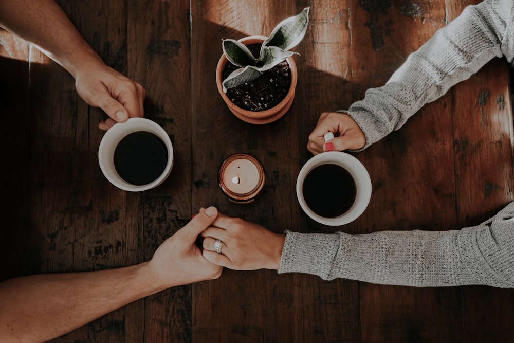 person holding white ceramic mugs