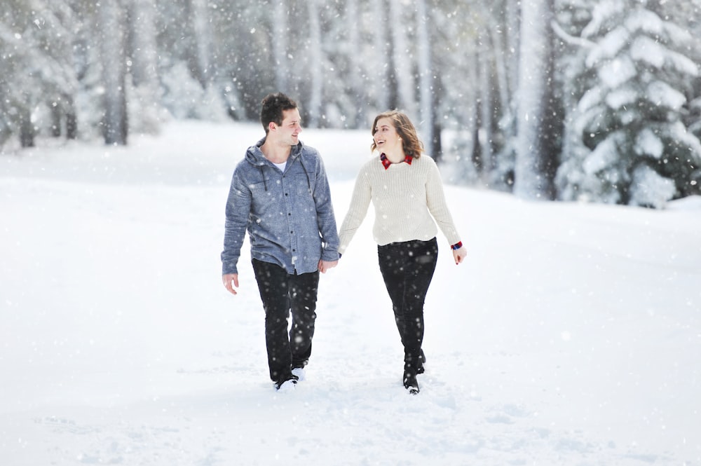 昼間、木のそばの雪の上を歩くカップル
