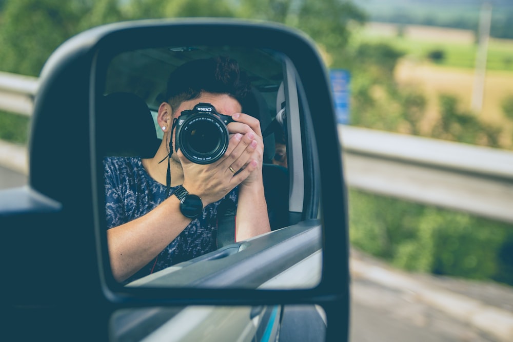 man taking picture on wing mirror