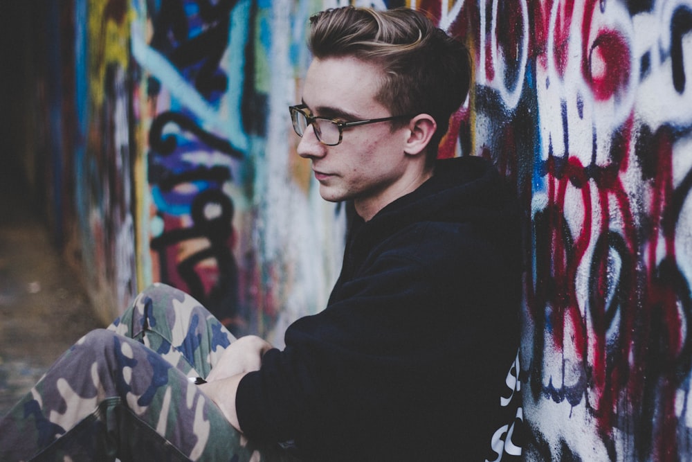 man wearing black hoodie and leaning on wall