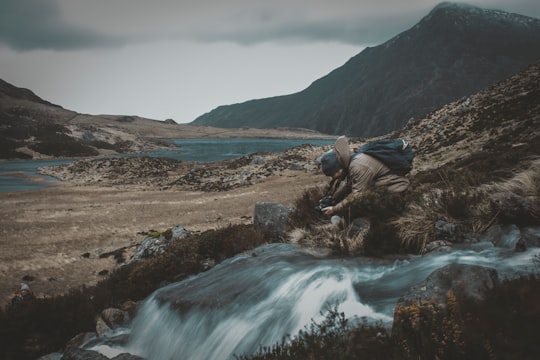man on ground beside river during daytime in Tryfan United Kingdom
