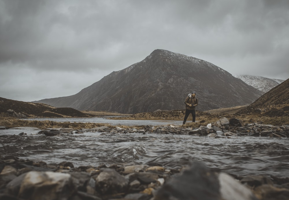 homme en manteau brun debout près de la rivière