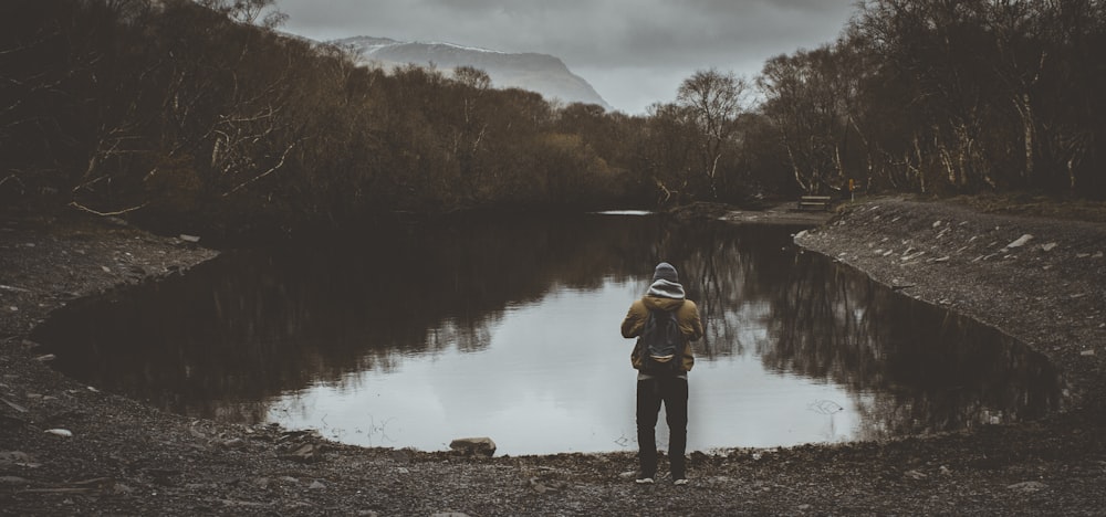 man standing front of lake surrounded by trees