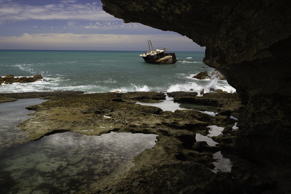 brown and white fishing vessel near rock formation