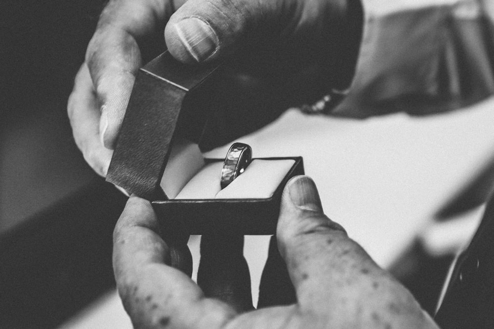 Graustufenfotografie einer Person, die einen silberfarbenen Ring in einer geöffneten Schachtel hält