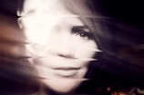 A distorted portrait of a person's face with a wave-like effect applied, causing blurring and blending of features. The image uses light and shadow to create an abstract, ethereal appearance.