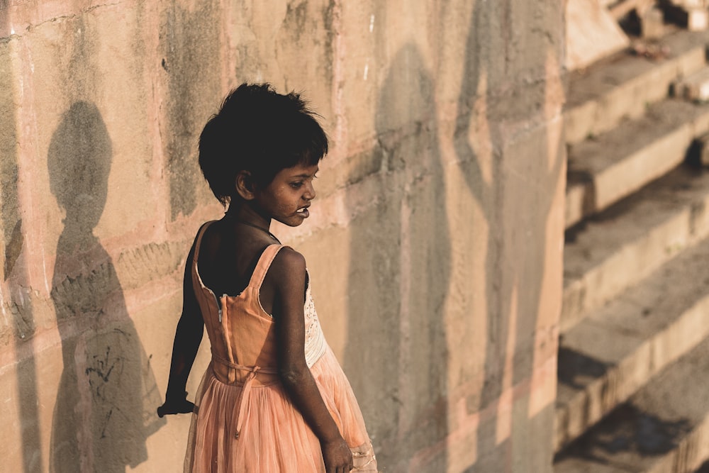 girl wearing beige sleeveless dress standing near wall