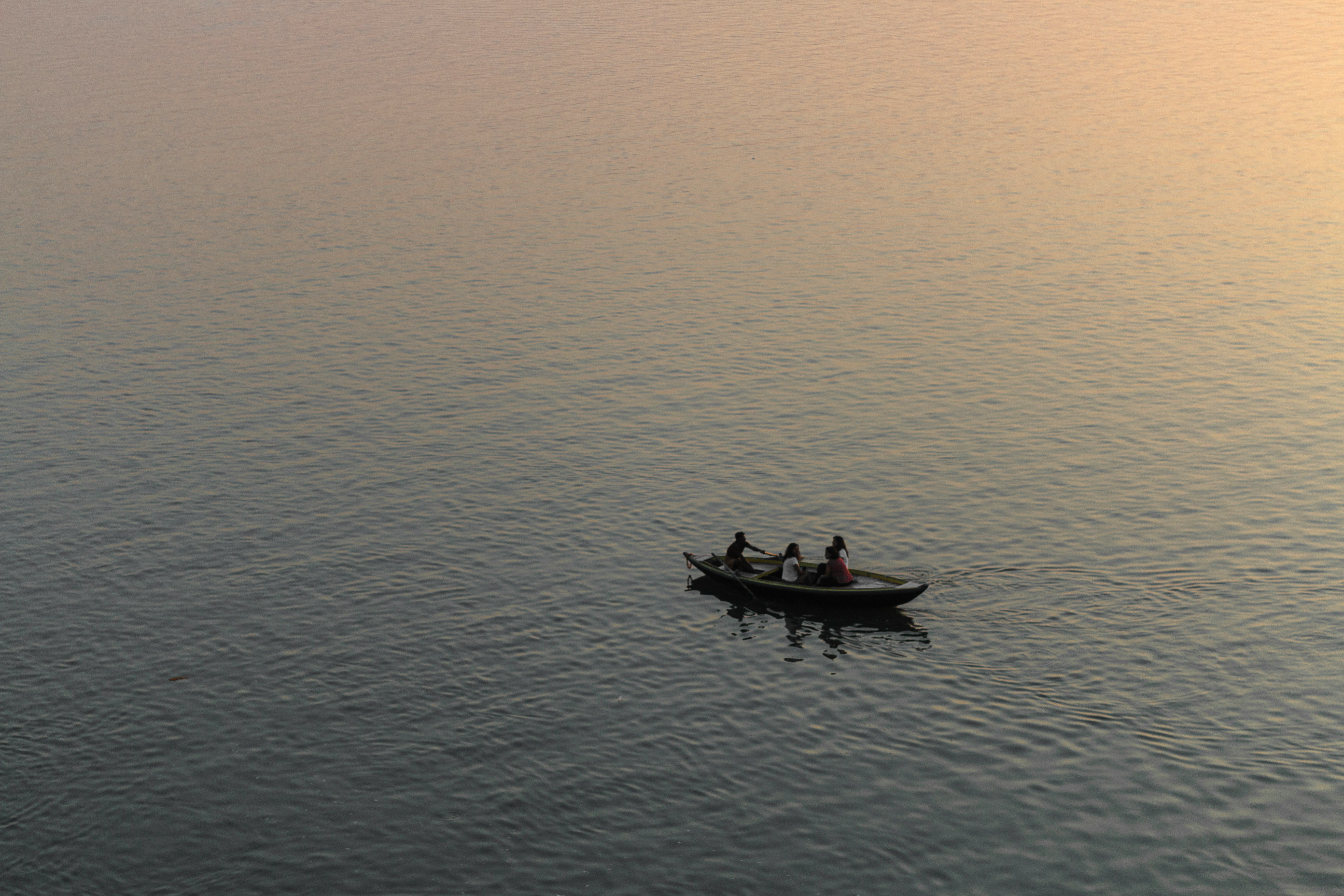 three person riding on boat surrounded by water during golden hour