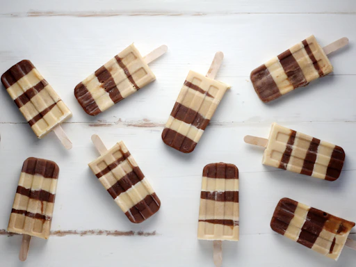 Close-up of colorful gourmet geladinho popsicles arranged on a rustic wooden table.