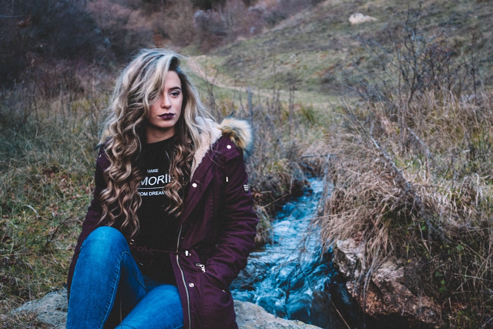 woman sitting on rock near body of water