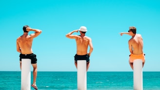 three men's sitting on white concrete bollard near body of water during daytime