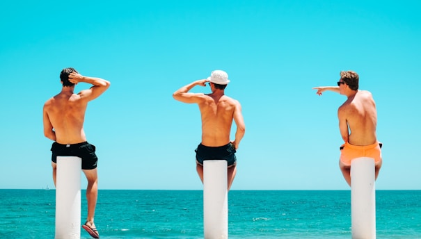 three men's sitting on white concrete bollard near body of water during daytime