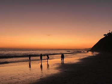 Sunset silhouette of a small group trekking a rugged cliff path with waves crashing below.