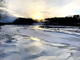 A frozen lake reflecting the soft glow of the setting sun with skaters enjoying the ice.