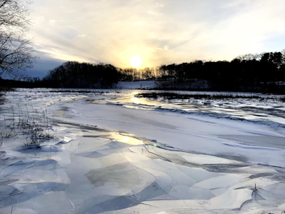 A frozen lake reflecting the soft glow of the setting sun with skaters enjoying the ice.