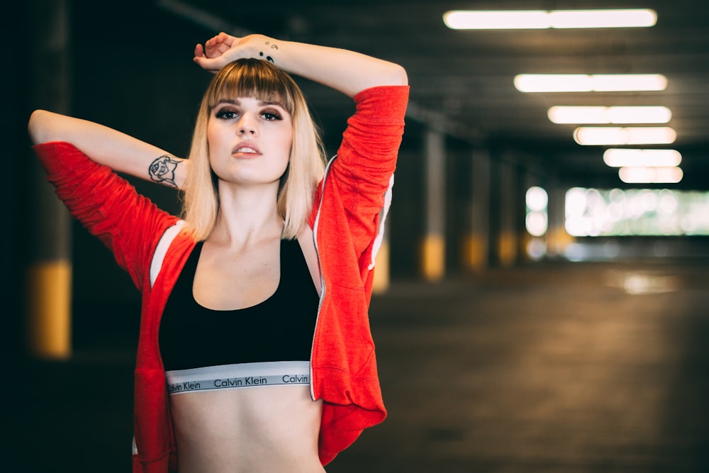woman in black sports bra and red jacket posing in parking lot