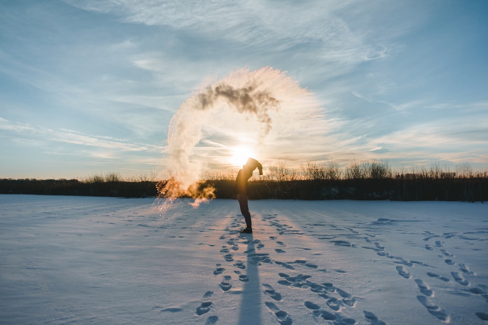 person standing on snowy ground spreading snow on air