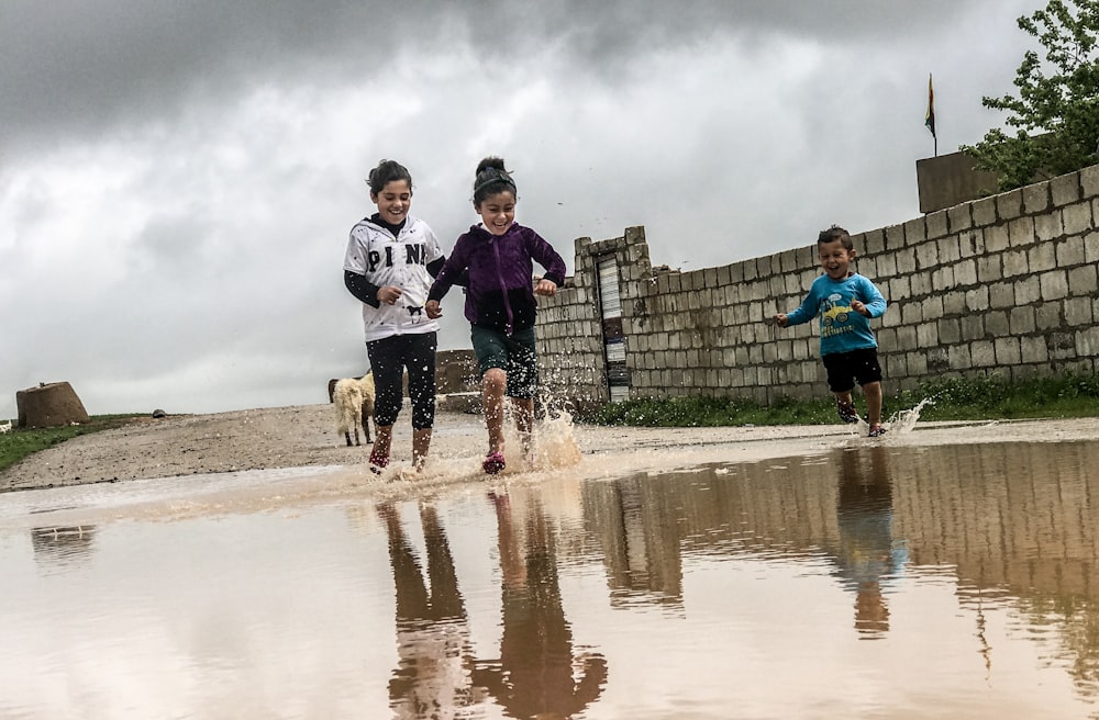 three children running towards body of water