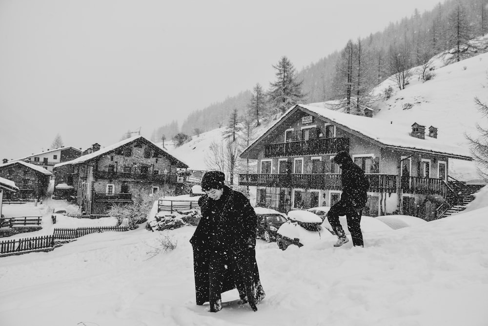 grayscale photo of man covered with coat near houses