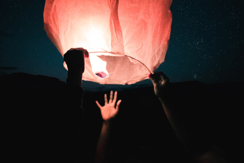 three human hand about to catch and hold sky lantern at night time