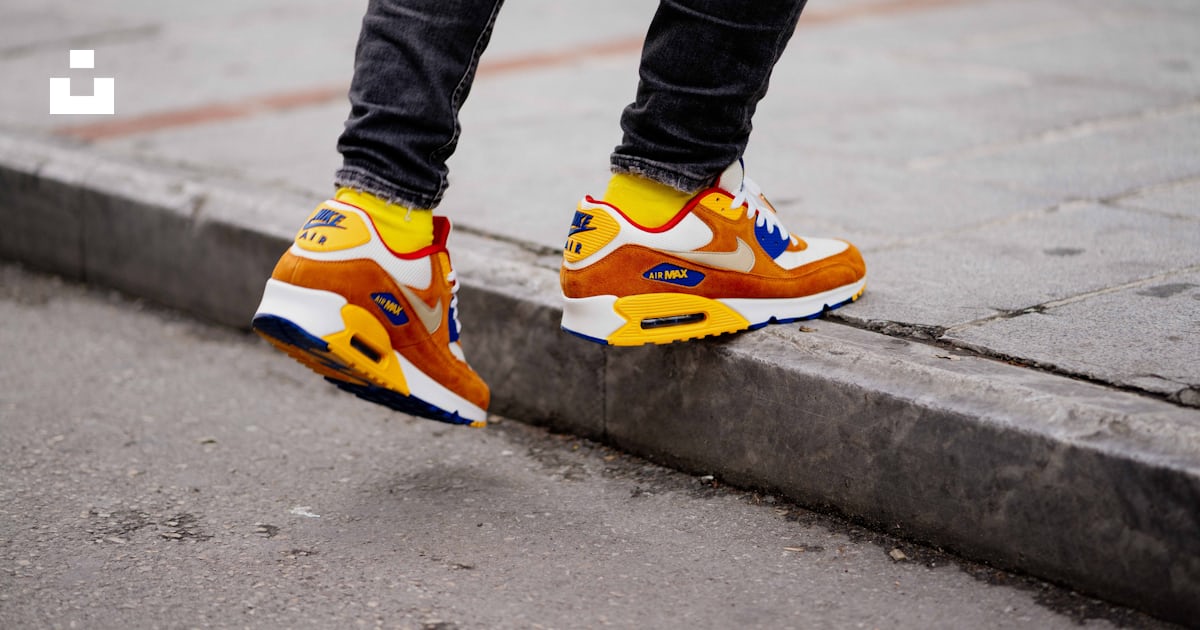 Person wearing pair of orange and white Nike Air Max low top shoes