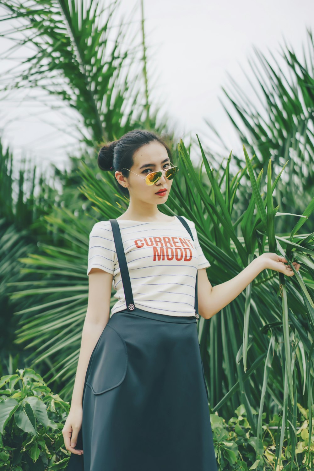 Mujer con top blanco de cuello redondo con falda de tirantes negros sosteniendo plantas