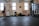 A person is performing a fitness exercise using battle ropes in a gym. The gym environment includes various types of equipment such as weights, resistance bands, and a squat rack. The floor is covered with black mats, and there are large windows allowing natural light. The walls have motivational text and there is a framed picture.