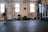 A person is performing a fitness exercise using battle ropes in a gym. The gym environment includes various types of equipment such as weights, resistance bands, and a squat rack. The floor is covered with black mats, and there are large windows allowing natural light. The walls have motivational text and there is a framed picture.