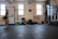 A person is performing a fitness exercise using battle ropes in a gym. The gym environment includes various types of equipment such as weights, resistance bands, and a squat rack. The floor is covered with black mats, and there are large windows allowing natural light. The walls have motivational text and there is a framed picture.