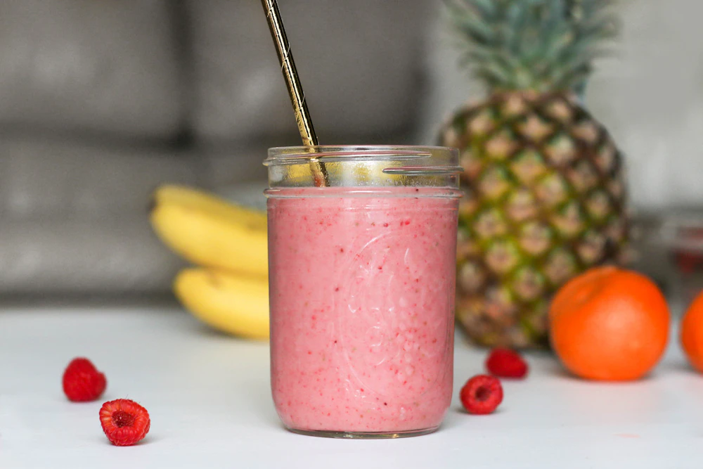 Pink raspberry smoothie in a glass jar with fresh fruit