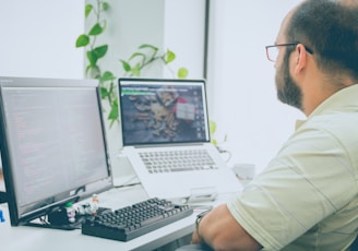 man sitting in front of computer monitor and laptop