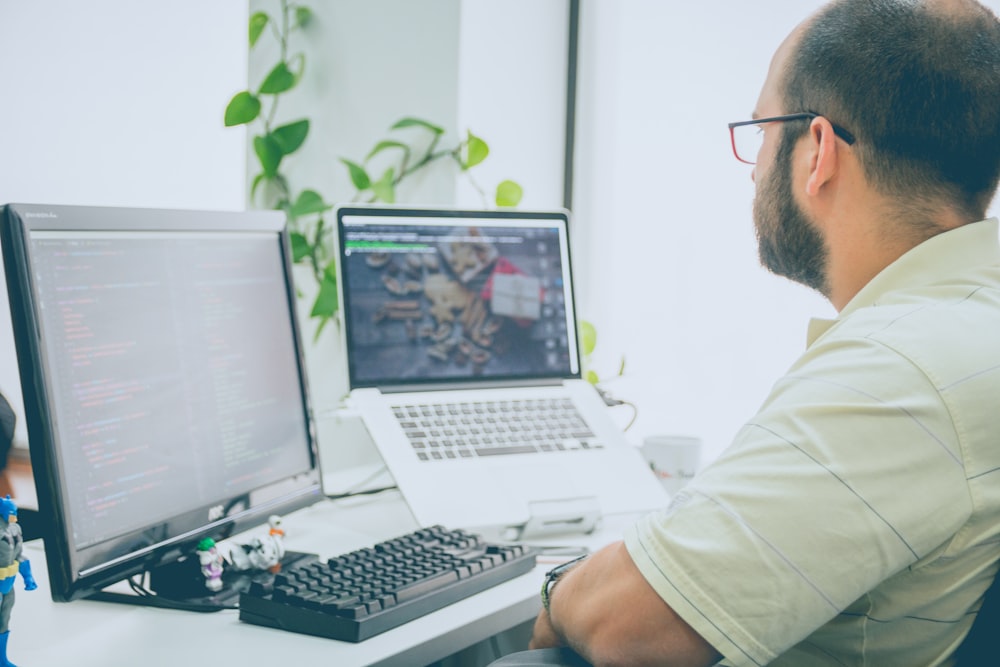 man sitting in front of computer monitor and laptop