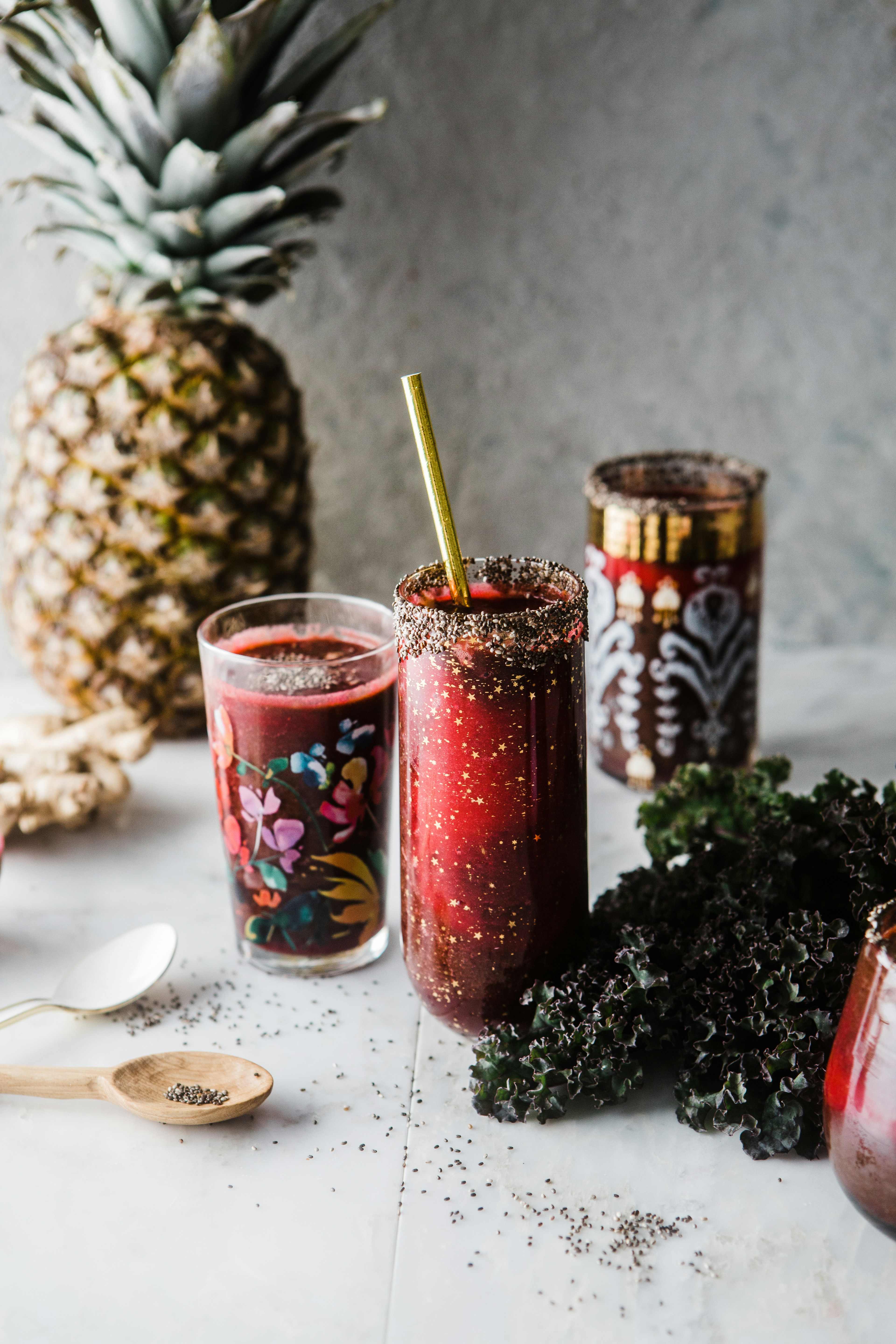 two drinking glass with red liquid near pineapple and green leaves
