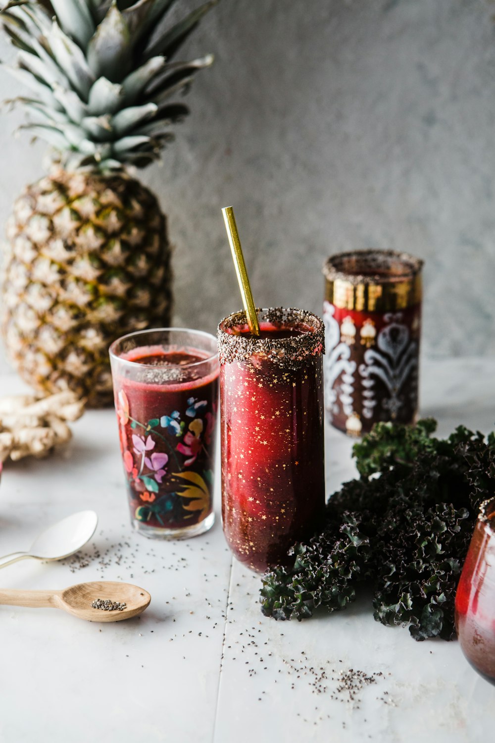 two drinking glass with red liquid near pineapple and green leaves