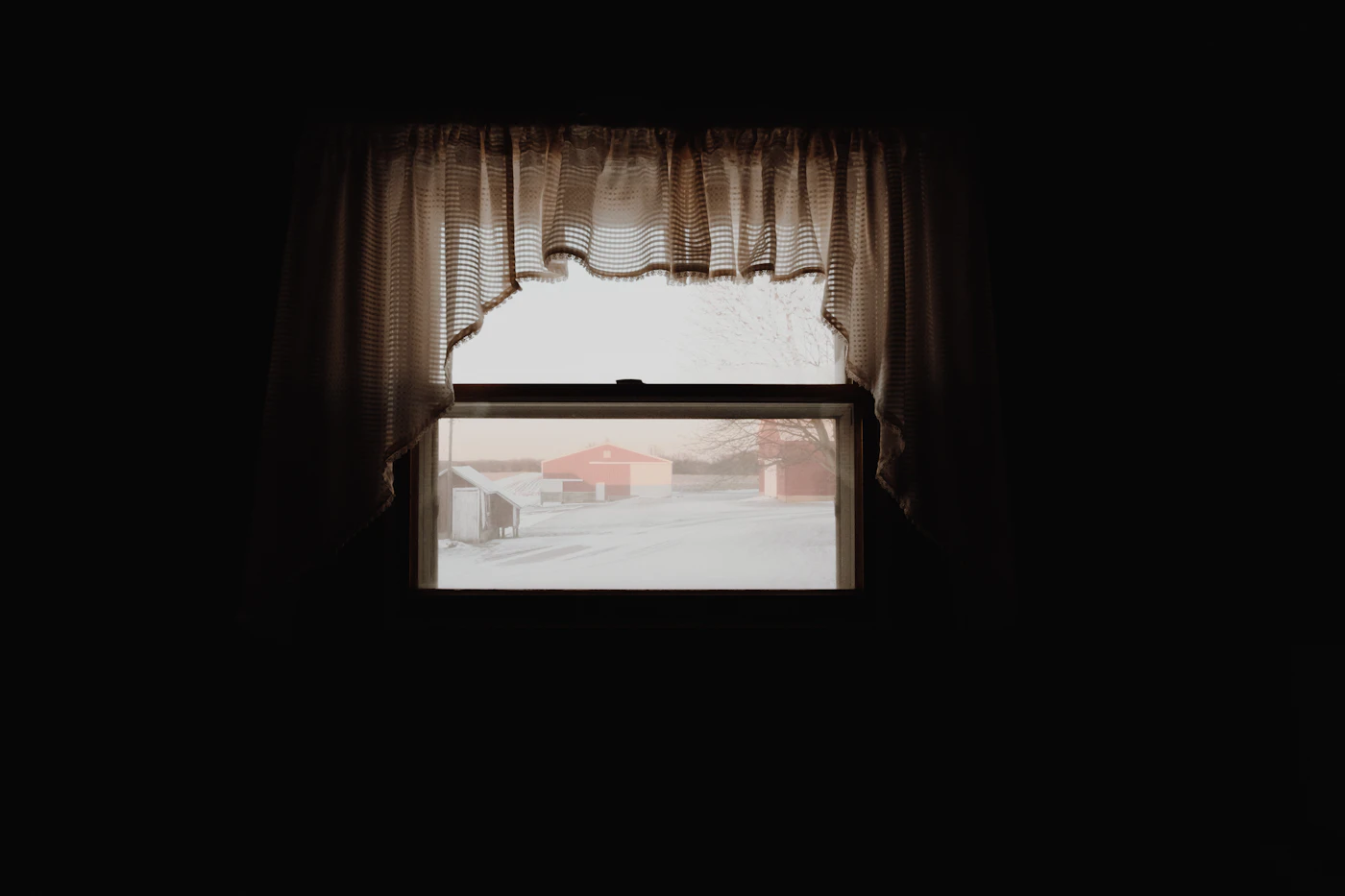 Fenster mit hellem Vorhang und Blick auf eine winterliche Landschaft