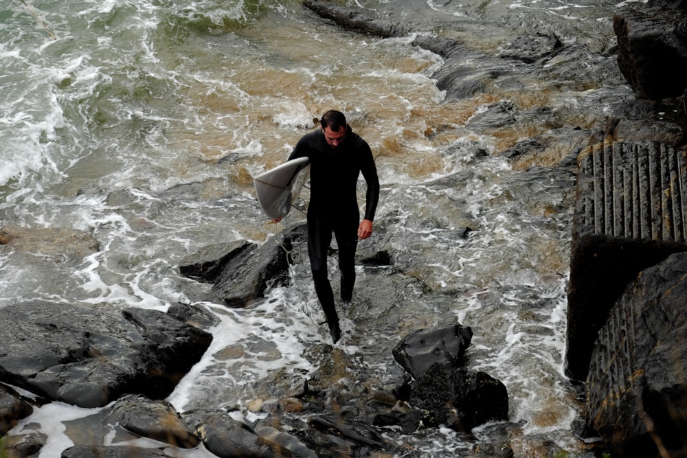 man holding white surfboard while walking on rocks