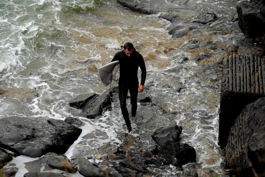 man holding white surfboard while walking on rocks