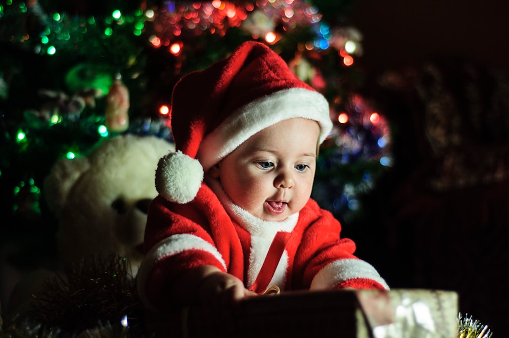 baby wearing Santa Claus outfit near Christmas tree